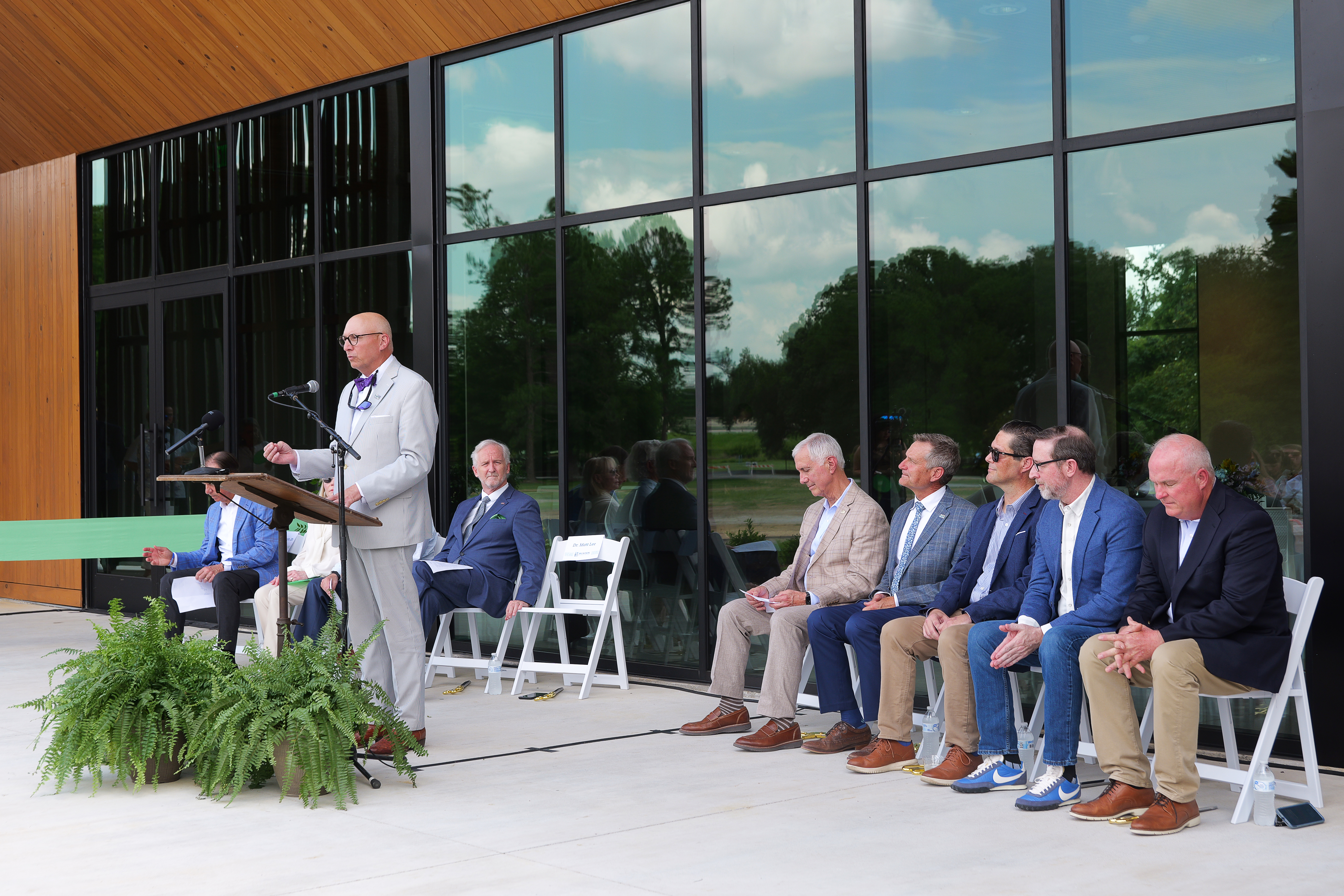 Man speaking at lectern with several people seated nearby.